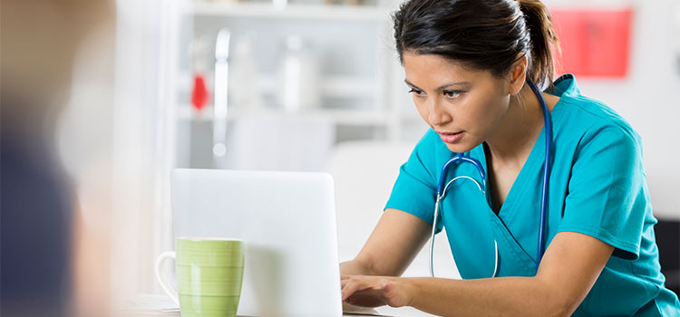 woman in scrubs typing on laptop