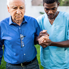 nurse holding arm of older man and assisting walk outdoors