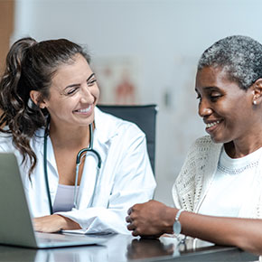 nurse in white coat with laptop at desk with smiling patient