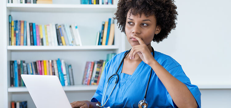 woman nurse contemplates while on laptop
