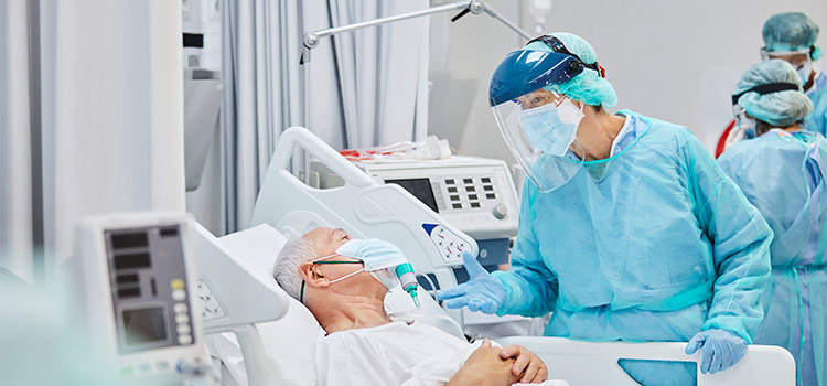 nurse with full protective equipment tends to patient in hospital bed