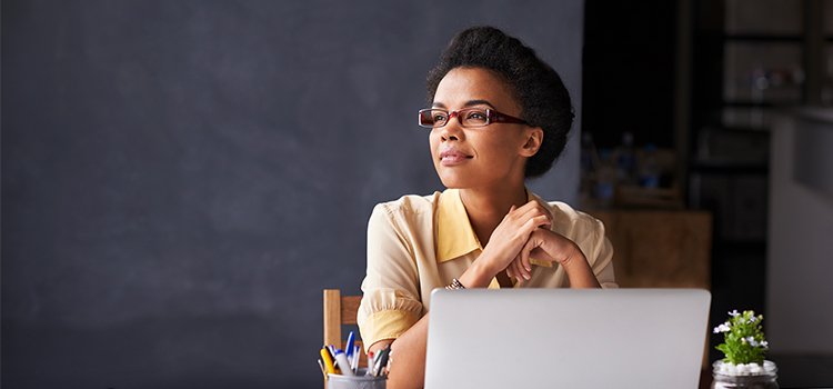 woman sitting at laptop computer looking away contemplatively