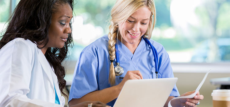 two nurses going over paperwork and working on laptop computer