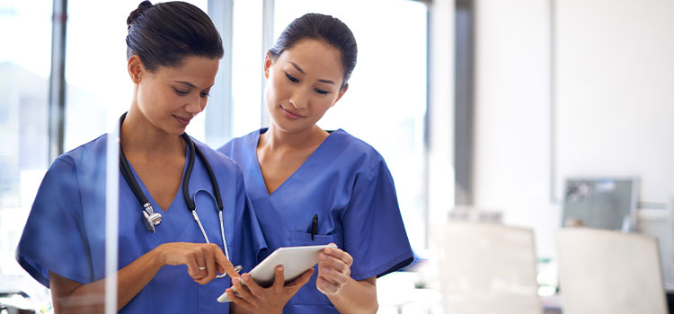 two registered nurses looking at electronic notepad