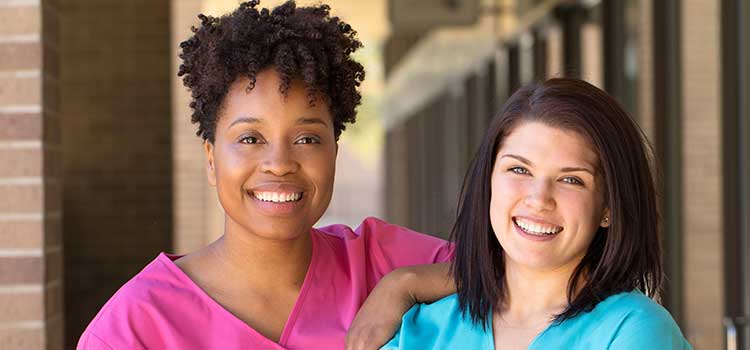 two female nurses in scrubs smile at the camera