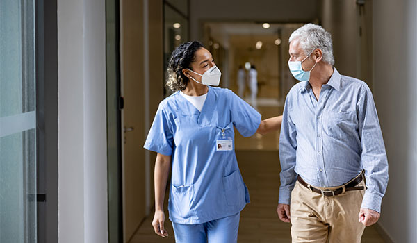 nurse navigator accompanies male patient in hospital hallway