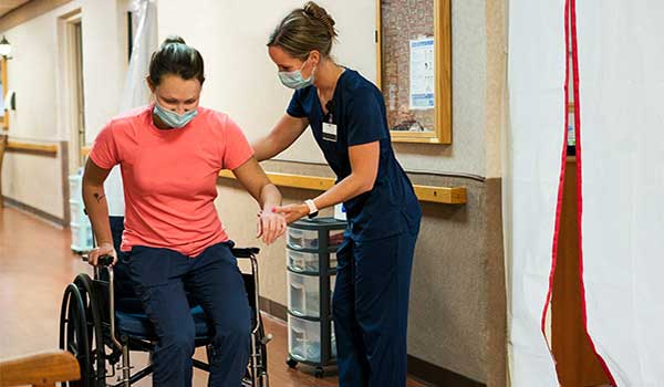 rehabilitation nurse helps patient stand up from wheel chair