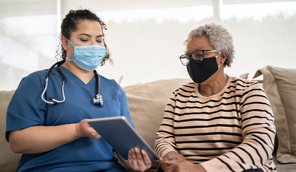 rural nurse in mask shows senior patient her chart on ipad