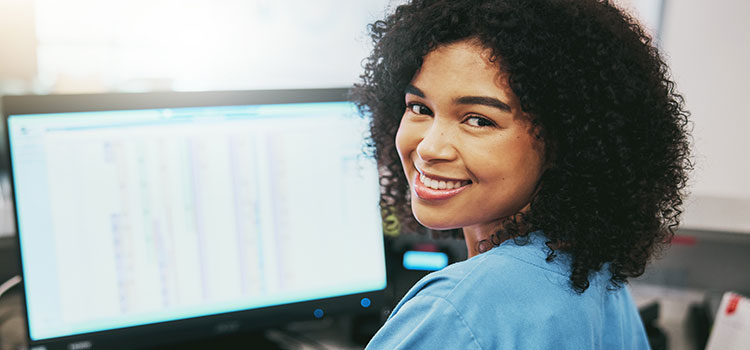 woman nurse works on desktop and smiles at camera