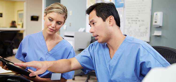 two nurses review patient roster at nurses station